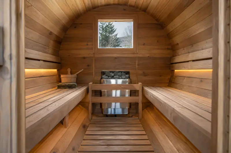 Inside a barrel sauna: facing benches and an electric heater at the far end
