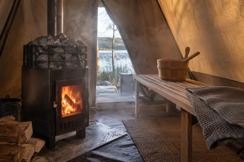 Inside a sauna tent: stove, stones and a folding bench